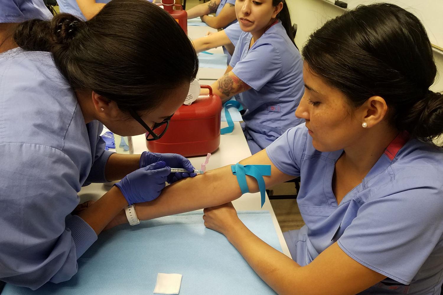 A medical assisting professor helps a student during a lab course.